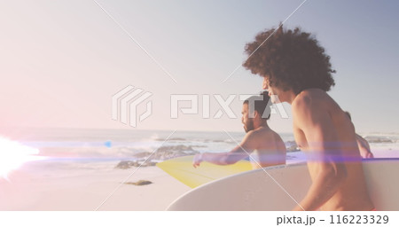 Image of light over happy diverse male friends running on beach with surfboards 116223329