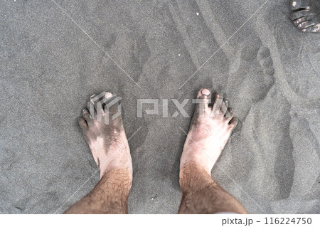 Bare foot on black sand, black volcanic beach barefoot person, dirty family feet on dark sea sand 116224750