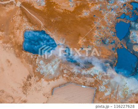 A stunning aerial view of a steaming blue geothermal pool surrounded by vibrant orange and white earth in Iceland, showcasing the country's natural beauty. 116227628