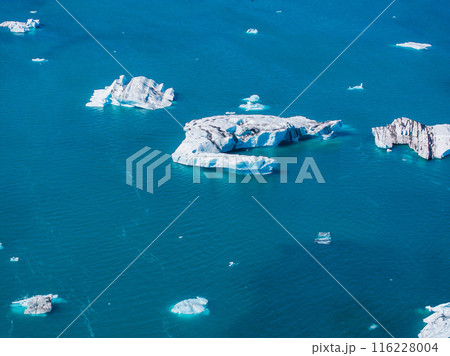 Stunning aerial view of calm turquoise waters with scattered white icebergs reflecting the clear blue sky in Iceland. A serene and breathtaking landscape. Stunning aerial view of calm turquoise waters with scattered white icebergs reflecting the clear blue sky in Iceland. A serene and breathtaking landscape. 116228004