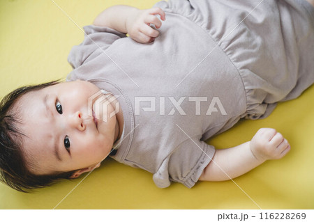 黄色バックに寝転ぶ女の子の赤ちゃん 黄色バックに寝転ぶ女の子の赤ちゃん 116228269