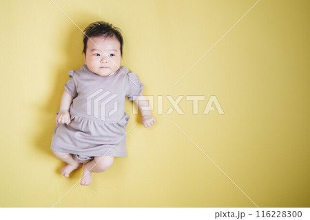 黄色バックに寝転ぶ女の子の赤ちゃん 116228300