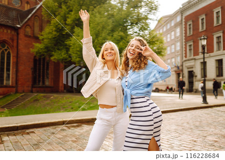 Smiling girlfriends are having fun on a sunny day on the streets of the city. Active lifestyle. 116228684