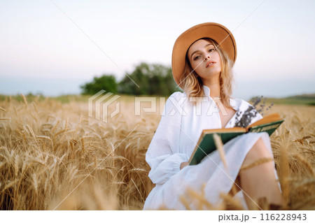 Young woman in white linen dress and hat enjoying a sunny day in a golden wheat field. Summer, beauty. 116228943