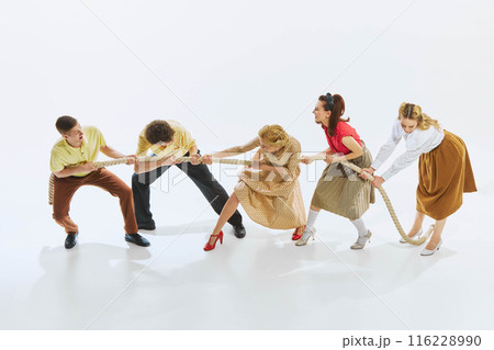 Group of men and women in vintage clothing engage in lively game of tug-of-war. People pulling rope, symbolizing competition and ambitions Group of men and women in vintage clothing engage in lively game of tug-of-war. People pulling rope, symbolizing competition and ambitions 116228990