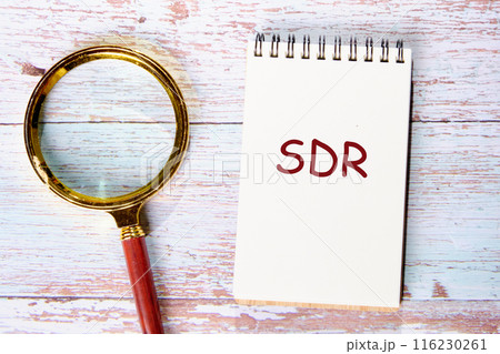 Business and SDR concept. Copy space. Special Drawing Rights. Word SDR. in a notebook next to a magnifying glass on old boards 116230261