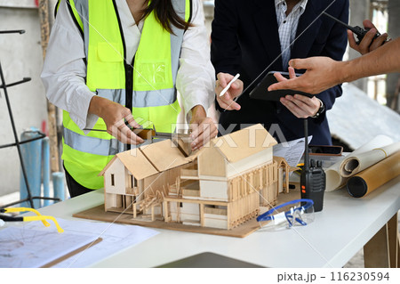 Engineers and businessman examining blueprints at table with architectural models in the foreground 116230594