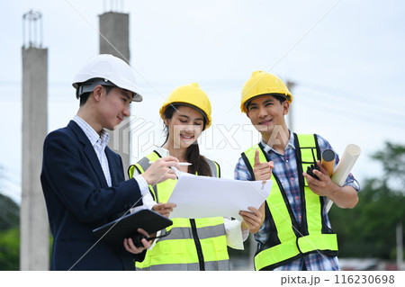 Construction professionals team and businessman in hard hats discussing on project at building site 116230698