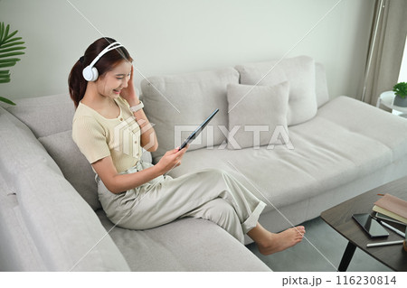 Smiling young woman wearing headphones enjoy watching video content on digital tablet Smiling young woman wearing headphones enjoy watching video content on digital tablet 116230814