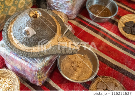 Traditional argan oil production setup, stone grinder, argan seeds, woven baskets, metal bowls, brown paste 116231627