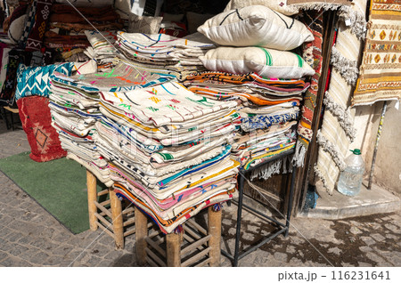 Colorful stacks of traditional Moroccan textiles and pillows on display at an outdoor market 116231641