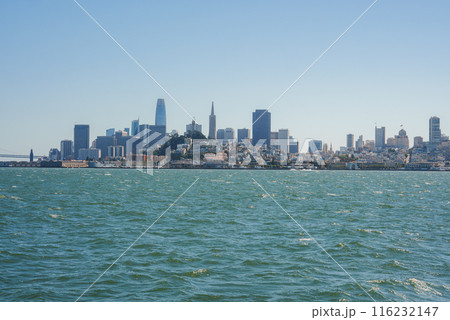 Panoramic view of San Francisco skyline from across the bay with city buildings creating a silhouette against a clear blue sky. No fog, iconic bridge, or boats in sight. Panoramic view of San Francisco skyline from across the bay with city buildings creating a silhouette against a clear blue sky. No fog, iconic bridge, or boats in sight. 116232147