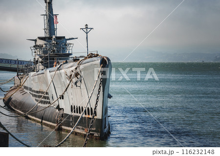 Large submarine moored at pier in calm bay waters. Hull number visible, tied with ropes. Overcast sky gives serene ambiance. Possibly San Francisco Bay area. perfect for tourists. Large submarine moored at pier in calm bay waters. Hull number visible, tied with ropes. Overcast sky gives serene ambiance. Possibly San Francisco Bay area. perfect for tourists. 116232148