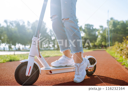 Young female legs on electric scooter. Woman rides electric scooter in park. Active lifestyle. 116232164