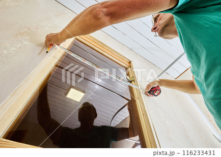 Measuring casing around door frame before nailing trim to jamb, joiner use tape measure and pencil. Measuring casing around door frame before nailing trim to jamb, joiner use tape measure and pencil. 116233431