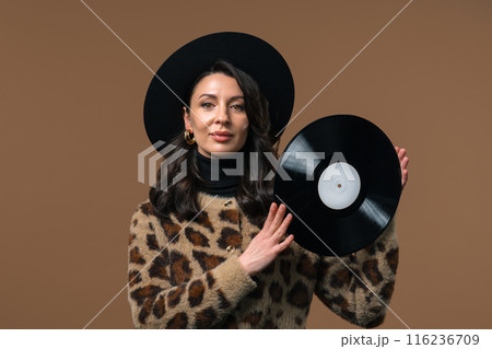 Stylish mature attractive woman with vinyl record disc on beige. Hobby, music lover, collection, nostalgia lifestyle 116236709