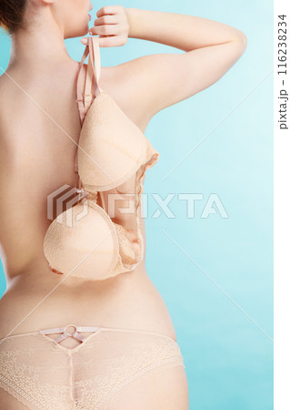 Naked woman holds beige bra in hand 116238234