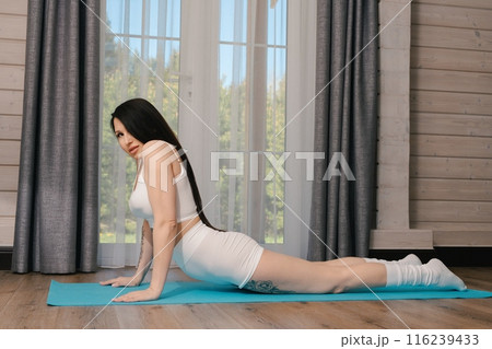 Woman Doing Yoga Pose in White Outfit Near Window Woman Doing Yoga Pose in White Outfit Near Window 116239433
