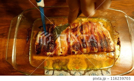A slice of pork tenderloin from the oven wrapped in strips of bacon. 116239703