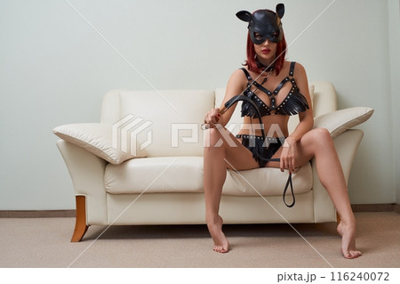 Domineering woman in sexy cat costume and mask sitting on sofa 116240072