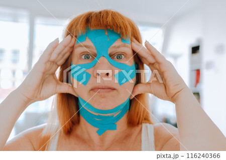 Close-up portrait middle-aged woman, she puts kinesiology tape on face Close-up portrait middle-aged woman, she puts kinesiology tape on face 116240366