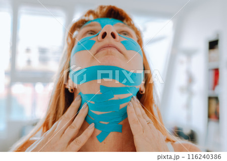 Close-up portrait middle-aged woman, she puts kinesiology tape on face Close-up portrait middle-aged woman, she puts kinesiology tape on face 116240386