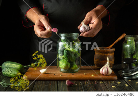 A man adds garlic to a jar of cucumbers before preserving them with spices. The concept of pickling vegetables in the kitchen at home 116240480