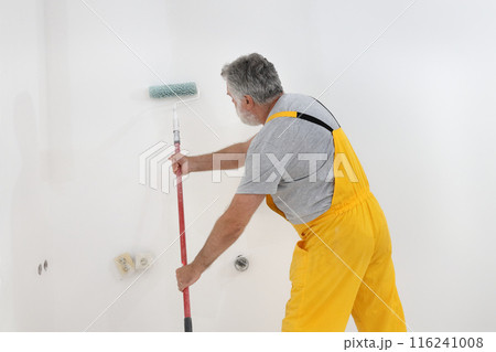 Adult worker paint wall in a room to white 116241008