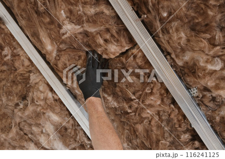 Worker hand in glove apply insulation for gypsum ceiling 116241125