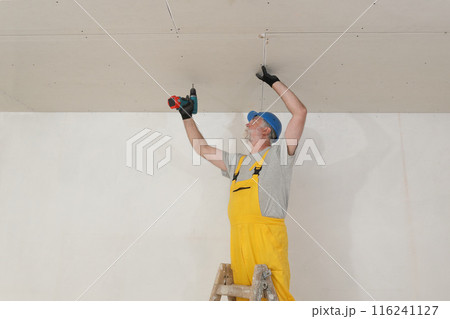 Senior adult worker fixing gypsum ceiling using screwdriver 116241127