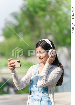 ヘッドホンを付けてスマホで動画を鑑賞する若い女性 ヘッドホンを付けてスマホで動画を鑑賞する若い女性 116246218