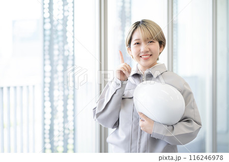 作業服を着てヘルメットを持つ金髪ショートヘアの若い女性(指さし、髪色自由、自分らしく働く、職場環境) 作業服を着てヘルメットを持つ金髪ショートヘアの若い女性(指さし、髪色自由、自分らしく働く、職場環境) 116246978