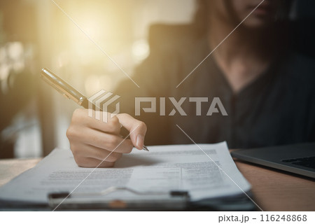 Woman hand holding a pen to sign a document or approval agreement contract on the desk. 116248868