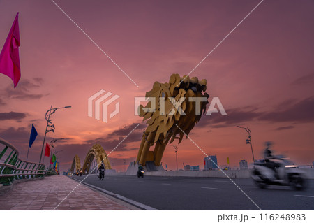 ベトナムダナン名物の夕方のドラゴンブリッジを走るオートバイや自動車 116248983