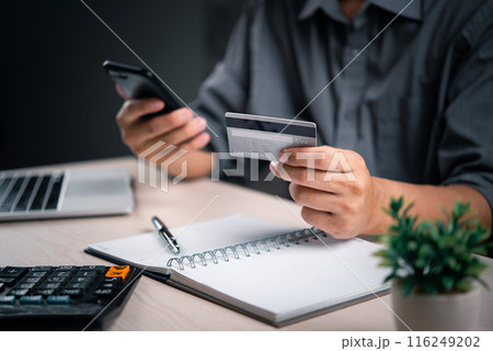 Man with credit card and smartphone finalizes a transaction, with a calculator and notepad nearby. online payment transaction e commerce shopping internet finance banking business concept. 116249202