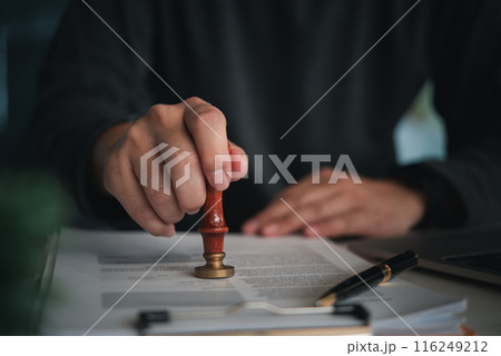 Focused individual placing a seal on an official document with red wax stamp in a professional setting 116249212