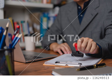 A professional applies an official seal to company documents, signifying authentication and approval. A professional applies an official seal to company documents, signifying authentication and approval. 116249313