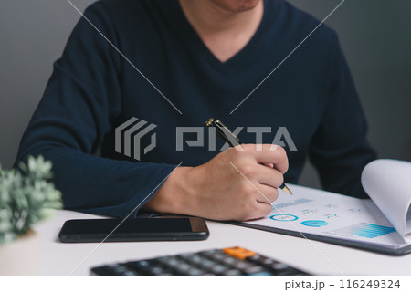 A business professional reviews analytical reports with, pen in hand. The scene captures the essence of strategic planning and performance assessment. 116249324