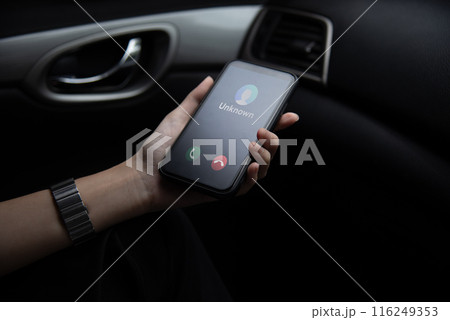 Hand holding a smartphone displaying an unknown caller ID Scam, fraud or phishing with smartphone inside a vehicle. 116249353