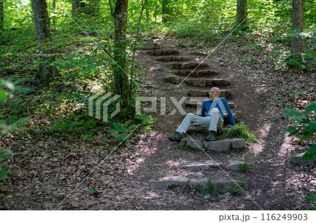 Physically fit senior man sits on woodland hiking trail steps thinking 116249903