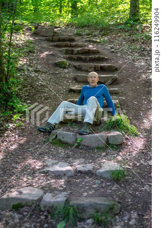 Physically fit senior man sits on woodland hiking trail steps thinking Physically fit senior man sits on woodland hiking trail steps thinking 116249904