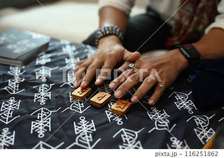 Fortune teller arrange wooden runes on a table covered with a mystical cloth. Forecasting and divination concept Fortune teller arrange wooden runes on a table covered with a mystical cloth. Forecasting and divination concept 116251862