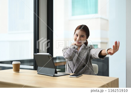 Happy relaxed young woman office worker sitting at desk with a laptop and stretching her arms 116251910