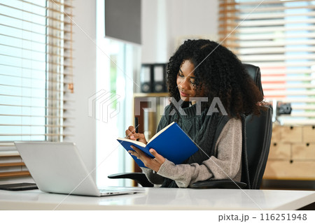 Young African American girl working with laptop and writing on notebook 116251948