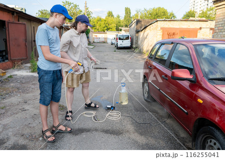 Dad and teenage son work together on the street near the garage. Outdoor activity. Family spend time. Helping and teach. Repairing a hose and pump for hand washing a car from a plastic bottle Dad and teenage son work together on the street near the garage. Outdoor activity. Family spend time. Helping and teach. Repairing a hose and pump for hand washing a car from a plastic bottle 116255041