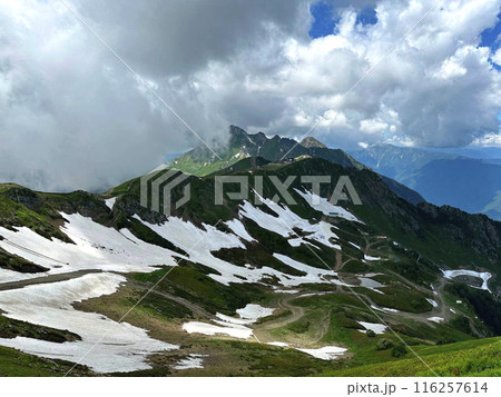View of the Mountains landscape. Green mountain slopes with snow. Grassy field and rolling hills 116257614
