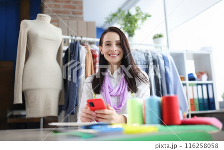 Smiling blooming woman holding smartphone at workplace Smiling blooming woman holding smartphone at workplace 116258058