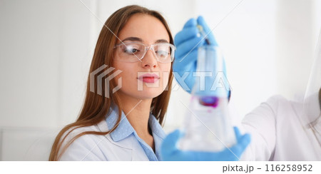 Scientist coworkers in glove add pink liquid to flask, microbiology science 116258952