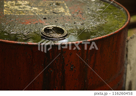 a metal red barrel stands on the street smeared with black liquid, dark oil runs down the barrel a metal red barrel stands on the street smeared with black liquid, dark oil runs down the barrel 116260458