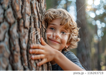 Selective focus of A Caucasian boy hugs the trunk of a big tree in the forest with a happy smile. 116263719
